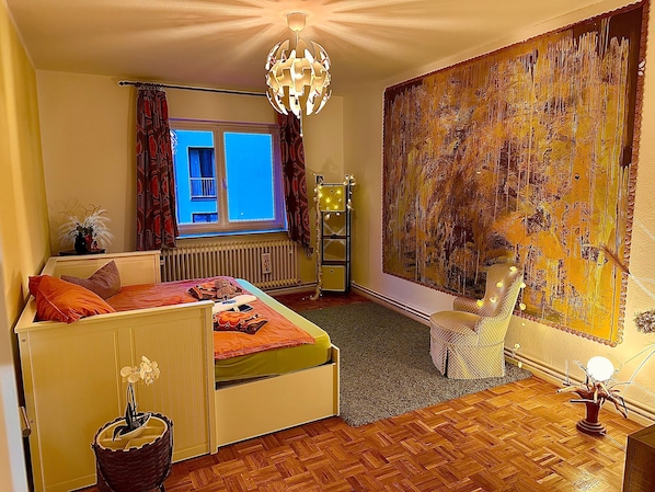 A bedroom with a bed, a window, a radiator, a lamp, and a painting on the wall.
