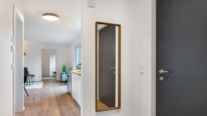 A hallway with wooden flooring, a dark door, and a mirror on the wall.