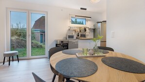 A modern kitchen with a microwave, oven, and sink, a dining area with a round table and chairs, and a sliding glass door leading to a garden.