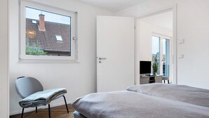 A bedroom with a large window, a bed, a desk, and a chair.