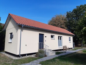 Une maison de plain-pied avec un toit recouvert de tuiles rouges, une porte d’entrée et un petit porche doté d’un banc.