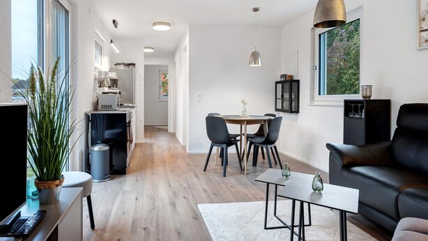 A modern living room with a sofa, a coffee table, and a dining area with chairs and a table.