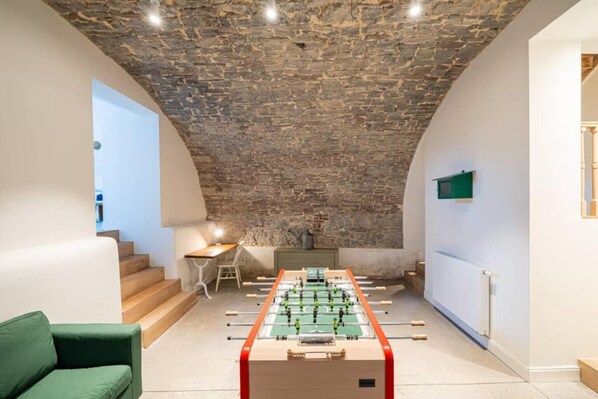 A room with a foosball table, a green sofa, and a staircase leading to a loft area.