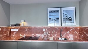 A modern kitchen with a marble countertop, a sink, and a faucet. There are two framed pictures on the wall above the countertop. - Edmond Vibes Almagro Suites (Madrid)