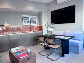 A modern kitchen with a marble countertop, a dining area with a black table and two chairs, a grey sofa, and a flat-screen TV mounted on the wall. - Edmond Vibes Almagro Suites (Madrid)