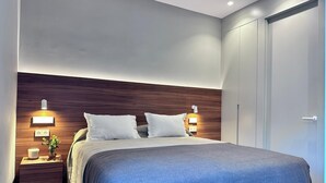 A modern bedroom with a wooden headboard, two bedside tables with lamps, a bed with a blue cover, and a wardrobe. - Edmond Vibes Almagro Suites (Madrid)