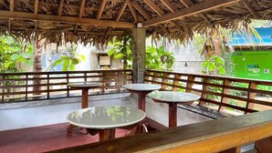 An outdoor patio with wooden tables and benches, a thatched roof, and a view of a green field. - Farmdean Holiday Home (Nagercoil)