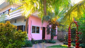 A pink building with a garden in front, including a palm tree and a red spiral sculpture. - Farmdean Holiday Home (Nagercoil)