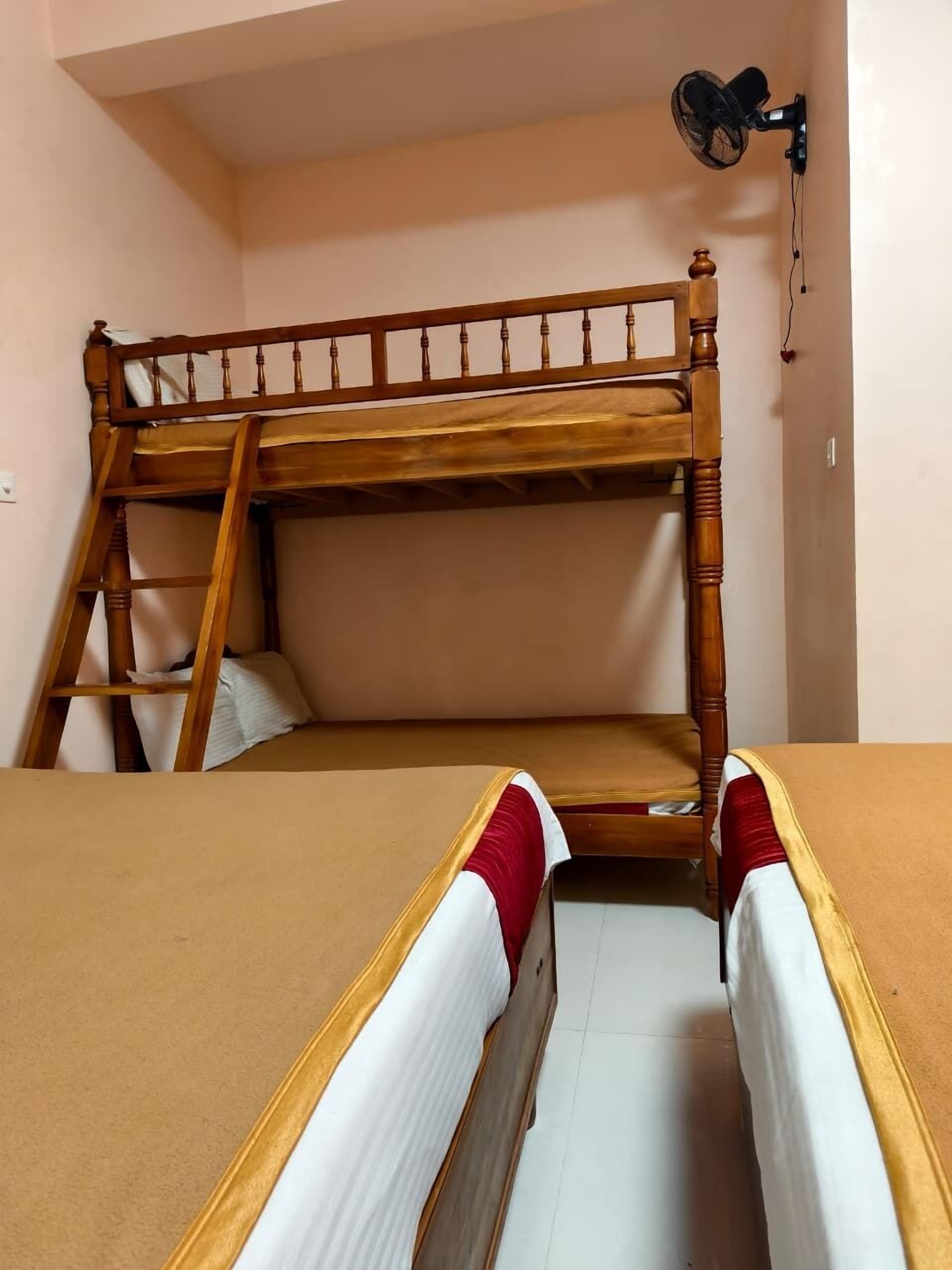 A bunk bed with a wooden frame and a ladder, a wall-mounted fan, and a plain wall.