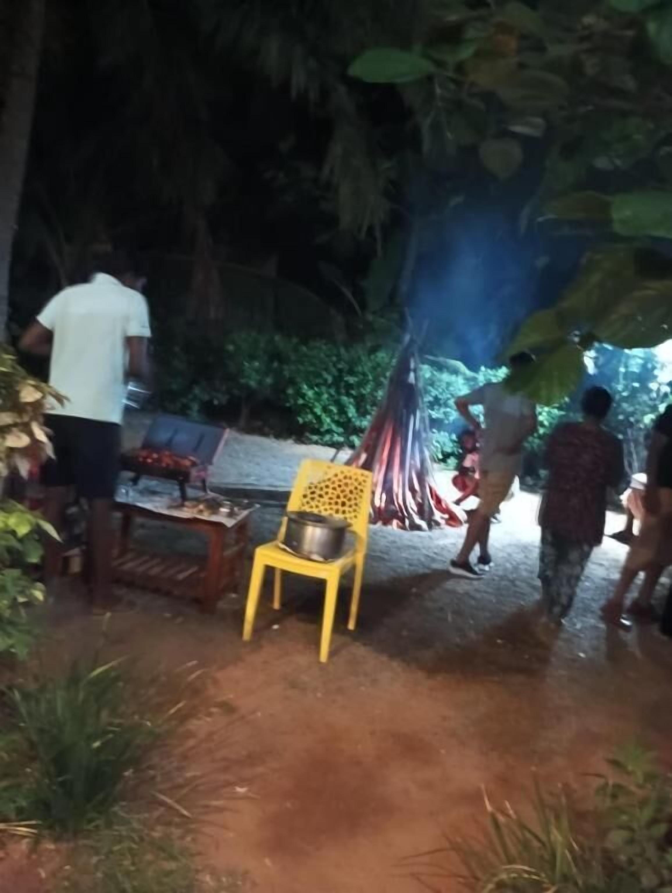 An outdoor area with a yellow chair, a table with a pot, and people gathered around.