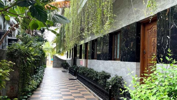 A corridor with checkered flooring, hanging plants, and a wooden door with intricate carvings. - Farmdean Holiday Home (Nagercoil)
