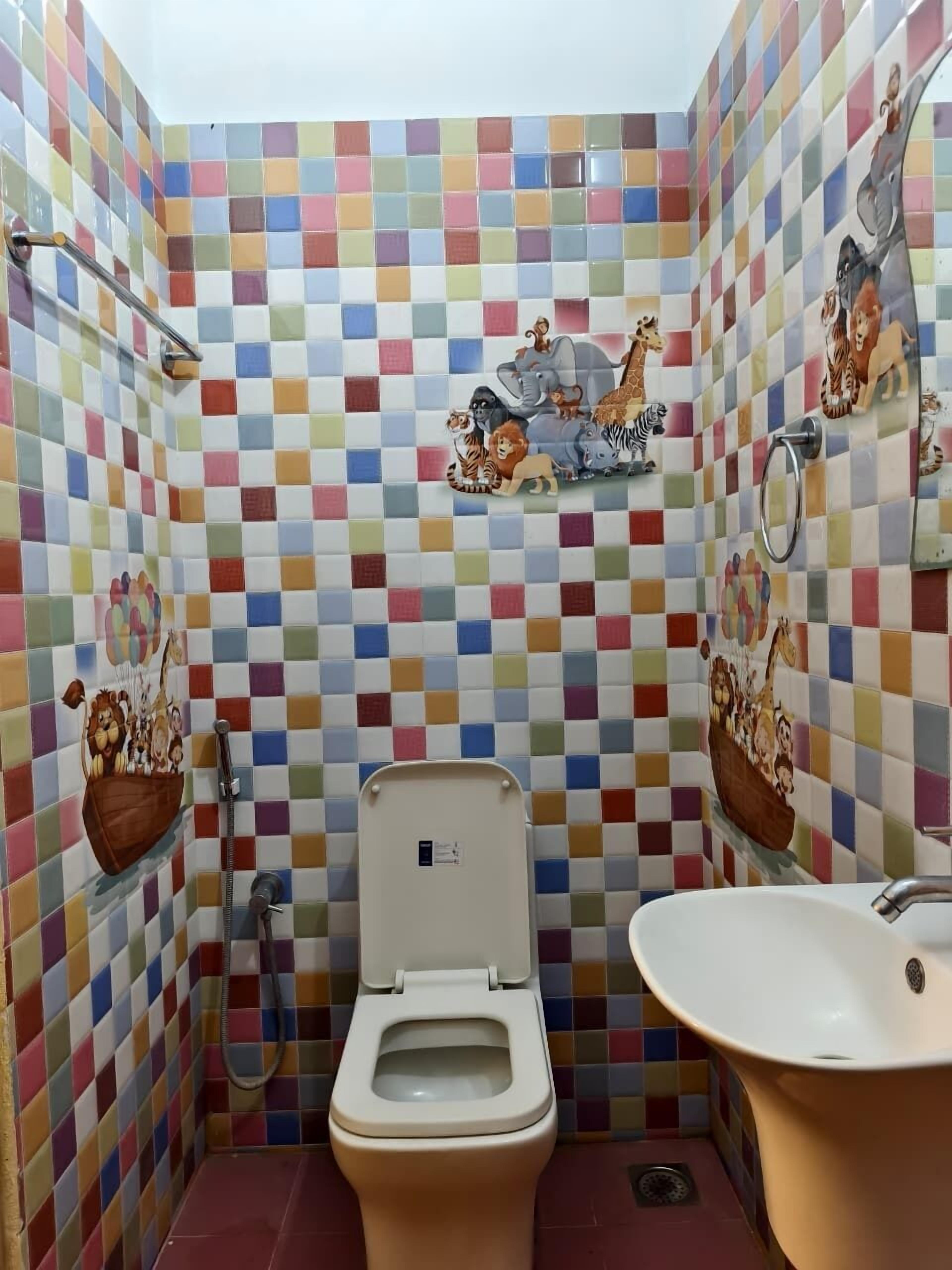 A bathroom with a colorful checkered tile wall, a toilet, a sink, and a shower with a glass enclosure.