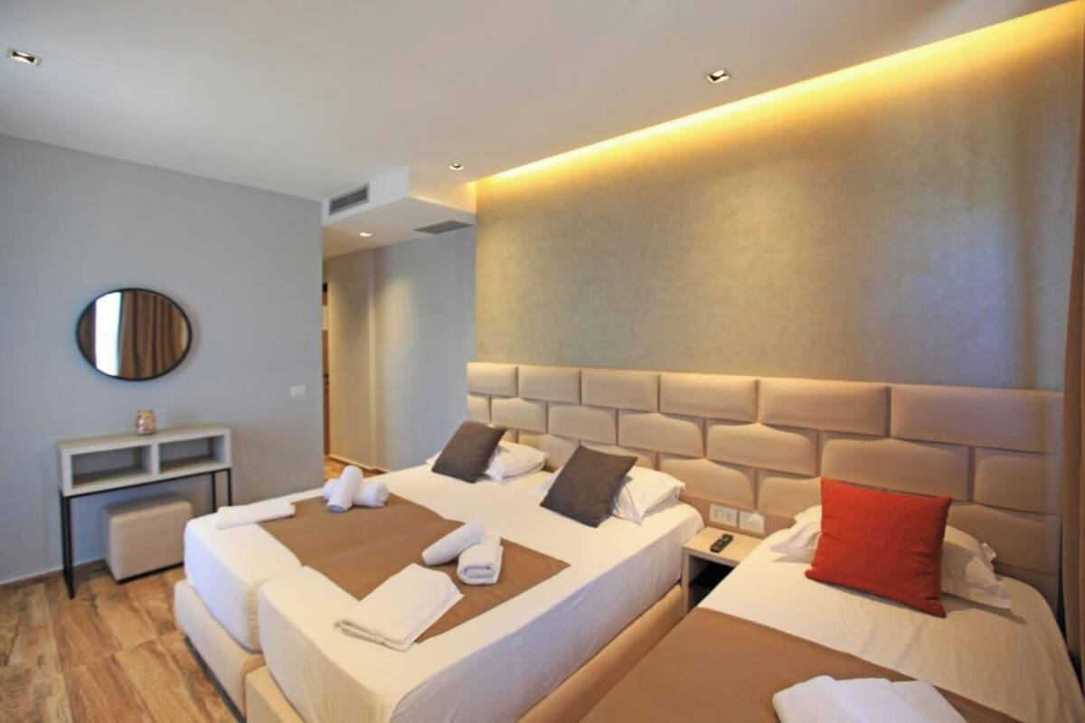 A hotel room with two beds, a bedside table, a mirror, and a wall-mounted light.