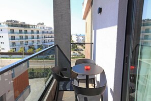 Un balcone con ringhiera in vetro, due sedie nere e un tavolino rotondo con un oggetto rosso sopra.