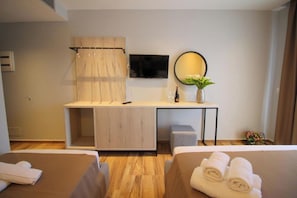 A hotel room with a bed, a desk with a chair, a TV, a mirror, and a small table with a vase of flowers. - Hotel Citrus (Ksamil)