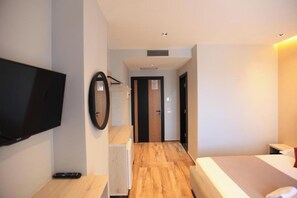 A hotel room with a bed, a TV mounted on the wall, a mirror, and a wooden floor.