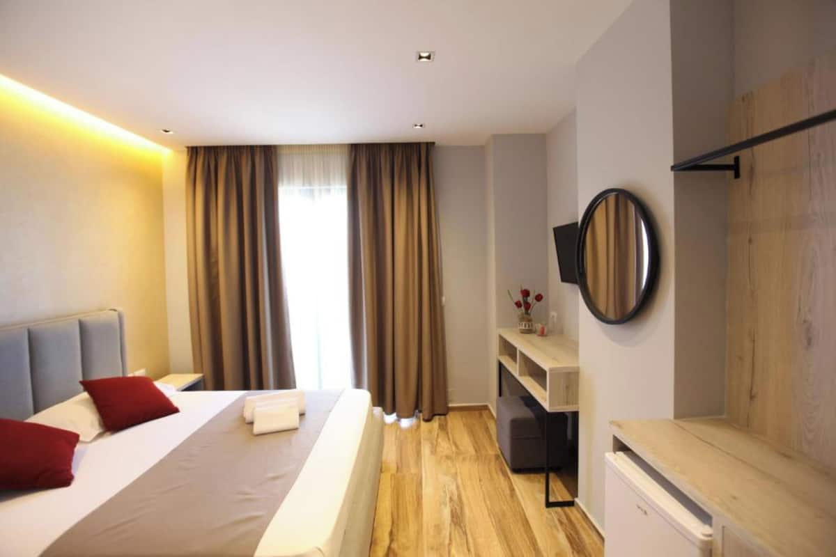 A modern hotel room with a large bed, a desk, a chair, and a flat-screen TV mounted on the wall.