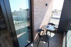 Ein Balkon mit Glastür, einem kleinen runden Tisch und zwei Stühlen, mit Blick auf Gebäude im Hintergrund.