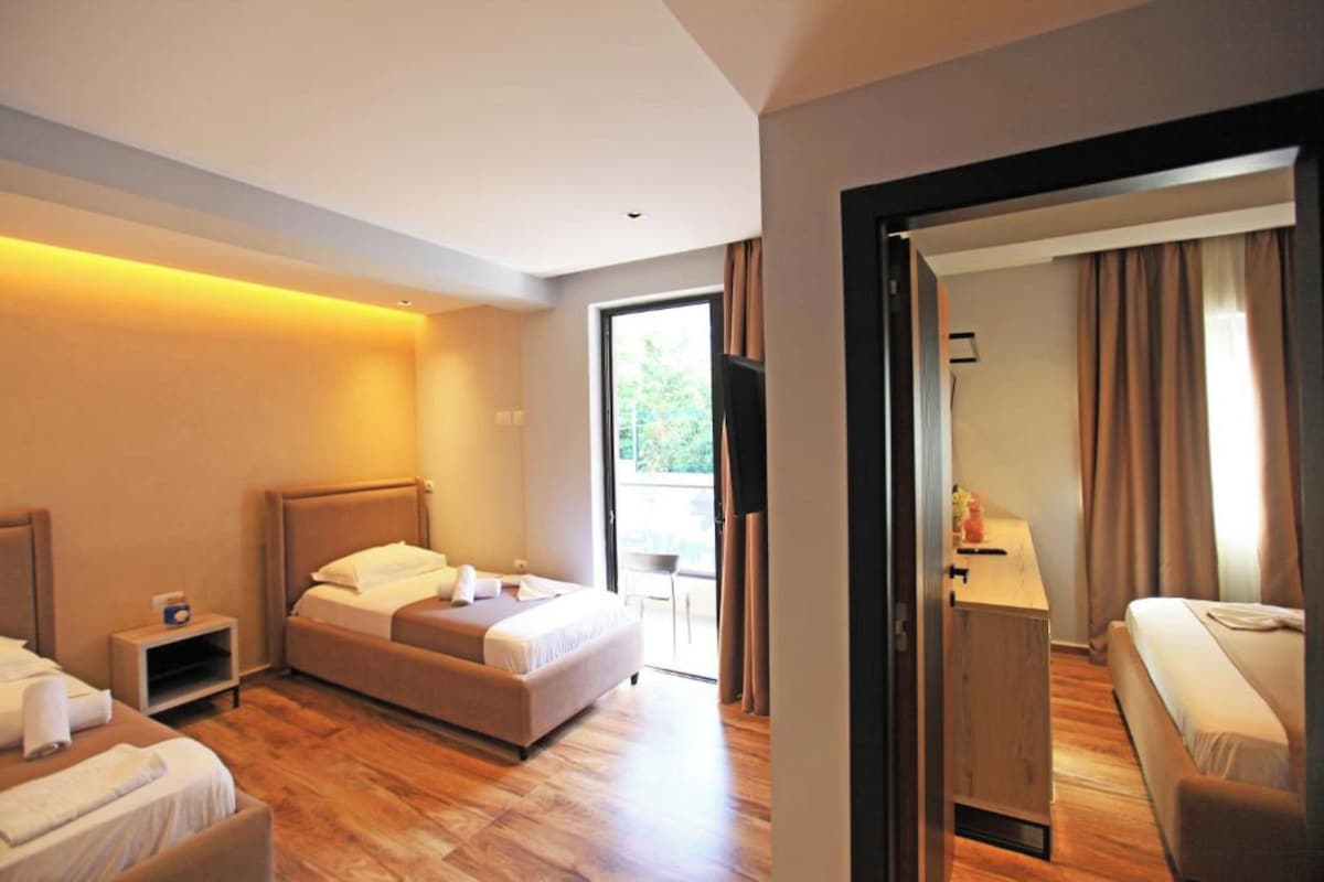 Ein Hotelzimmer mit Bett, Schreibtisch und Stuhl. Ein Fenster mit Vorhängen bietet Blick auf Grünfläche.