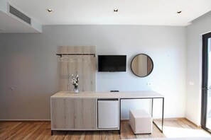 A modern, minimalist room with a wooden cabinet, a small fridge, a bench, a flat-screen TV, and a large mirror. - Hotel Citrus (Ksamil)