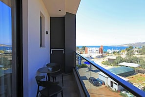 A balcony with a table and chairs, overlooking a coastal area with buildings and a clear sky. - Hotel Citrus (Ksamil)