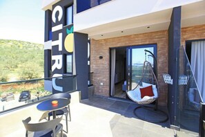 Un balcon moderne d’hôtel, agrémenté d’un fauteuil suspendu, d’une table et offrant une vue sur le paysage environnant.