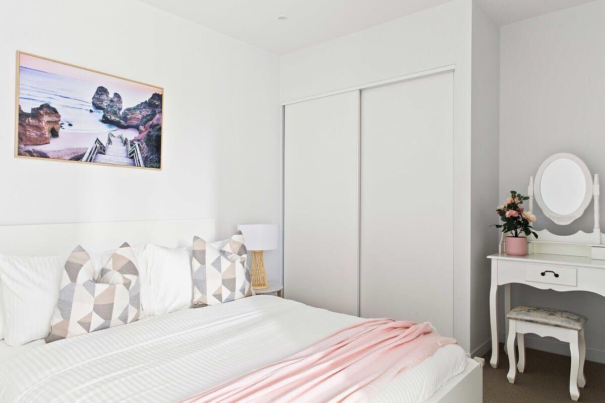 A bedroom with a bed, a dresser with a mirror, a bench, and a picture on the wall.