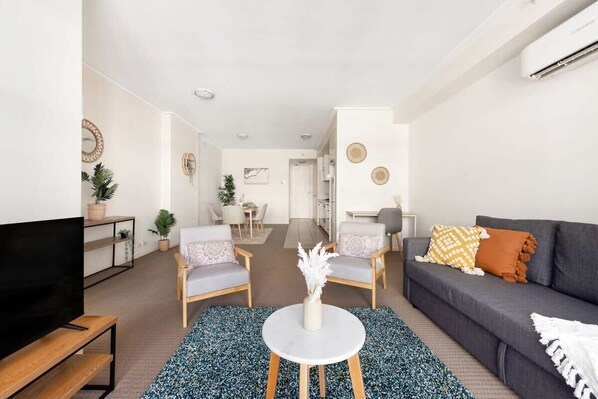 A modern living room with a sofa, two armchairs, a coffee table, and a TV. There is a kitchen area in the background. - A Plush & Comfy Apt Right Next to Darling Harbour (Sydney)