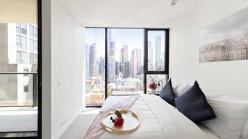 Quarto moderno com vista para a cidade, uma cama grande e uma mesa de cabeceira com bandeja.