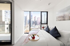Een moderne slaapkamer met uitzicht over de stad, een groot bed en een nachtkastje met dienblad.
