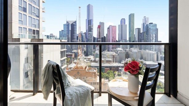 Ein Balkon mit Blick auf die Stadt, ein Sessel, ein Tisch mit Blumen und eine Jacke, die an der Reling hängt.