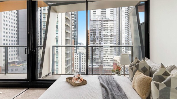 Ein modernes Schlafzimmer mit großem Fenster, einem Bett mit gemusterten Kissen und einer dekorativen Ablage am Fensterbrett.