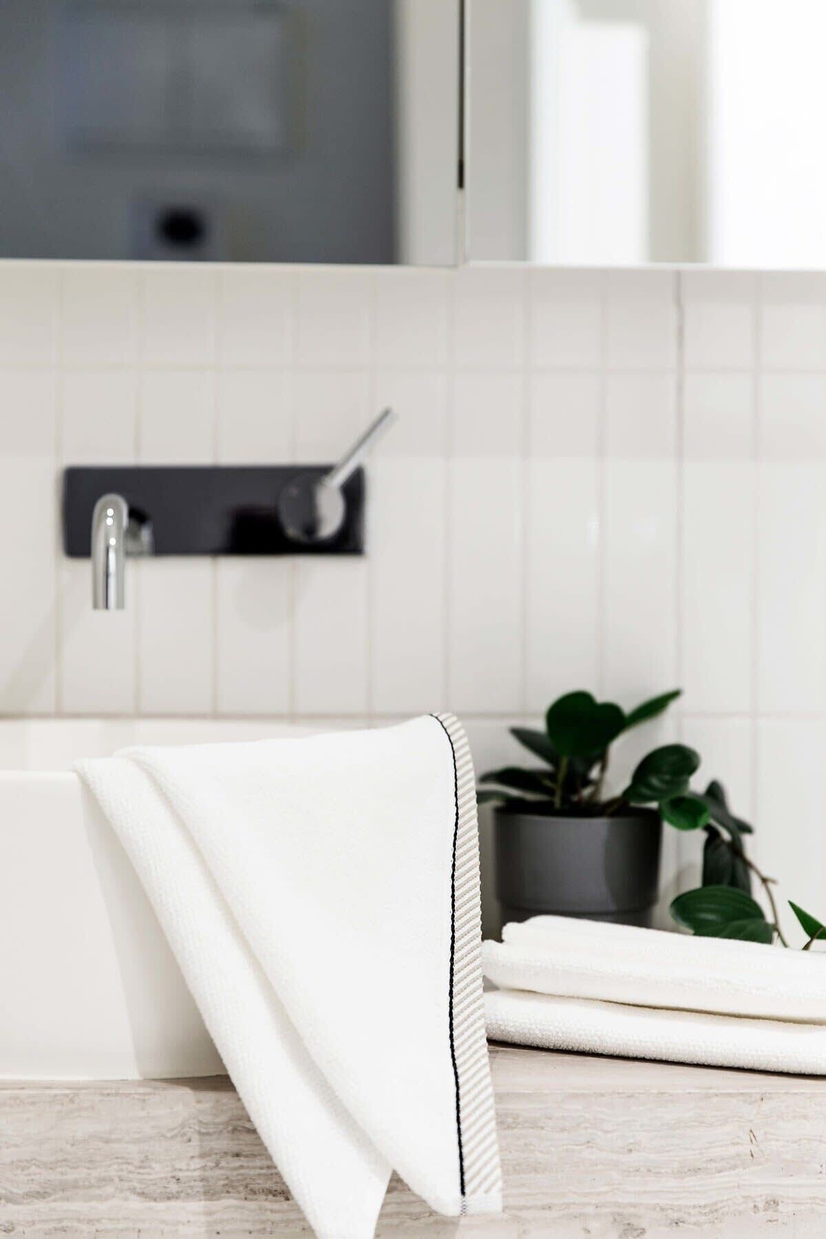 Un baño con lavamanos blanco, toallero e planta en maceta.