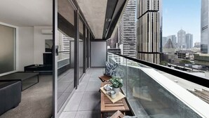 Un balcó modern amb vista al perfil urbà de la ciutat, que inclou una taula de fusta amb una planta, una banca i una barana de vidre.