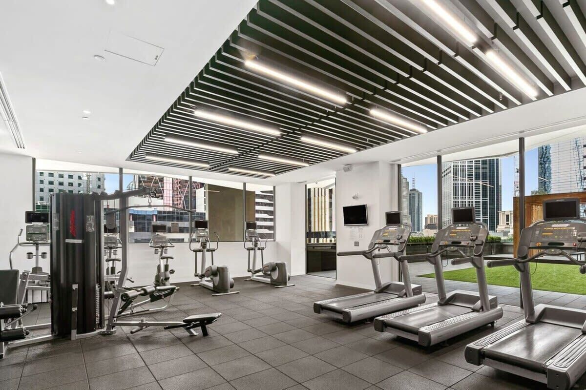 Ett modernt gym med löpband, styrketräningsmaskiner och ett stort fönster med utsikt över staden.