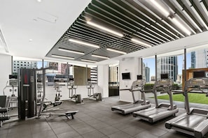 Une salle de sport moderne équipée de tapis de course, d’appareils de musculation et dotée d’une grande fenêtre offrant une vue sur la ville.