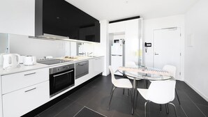 Een moderne keuken met een grote flatscreen televisie, een inbouwoven en een eethoek met een glazen tafel en witte stoelen.
