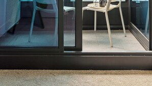 A balcony with a chair, a small table with a vase and a cup, and a view of the cityscape through large glass doors. - A Modern & Cozy 2BR Apartment With City Views (Melbourne)