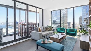 A modern living room with large windows, a grey sofa, teal armchairs, and a coffee table.