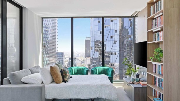 A modern bedroom with a large window, a bed, a green sofa, a bookshelf, and a desk with a plant.
