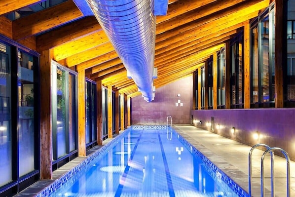 A long indoor swimming pool with wooden beams and glass walls.