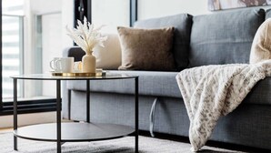 A modern living room with a grey sofa, a round black table with a white vase and a tray, and a grey blanket draped over the sofa. - Modern 2BR Apt Next to Southern Cross Free Parking (Melbourne)