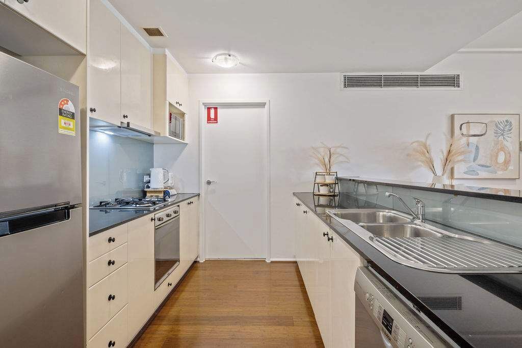 A modern kitchen with white cabinets, a stainless steel refrigerator, a built-in oven, and a dishwasher.