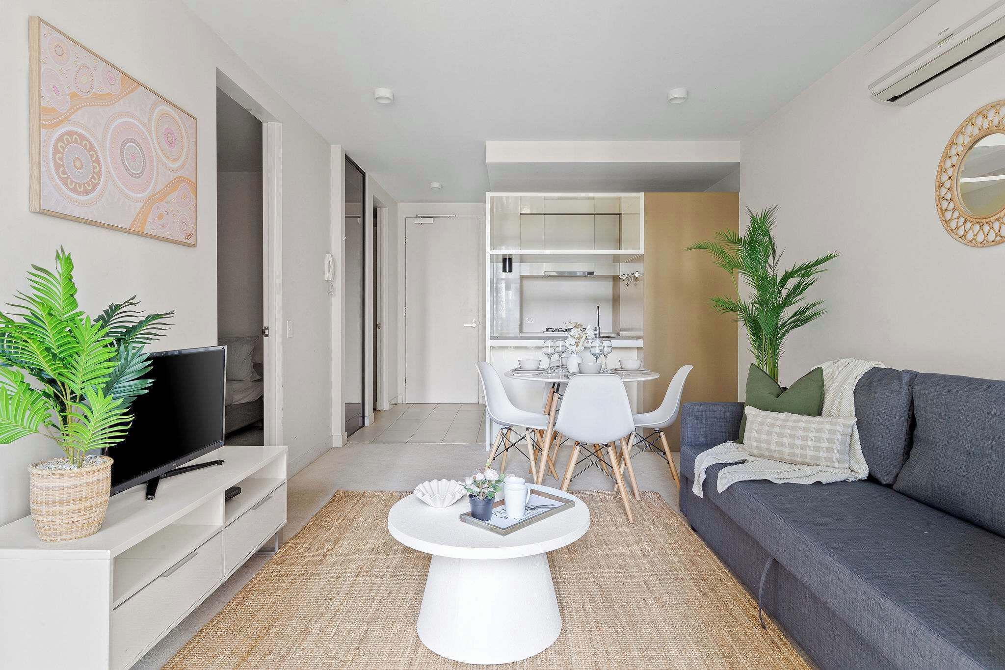 A modern living room with a flat-screen TV, a coffee table, a sofa, and a dining area with chairs and a table.