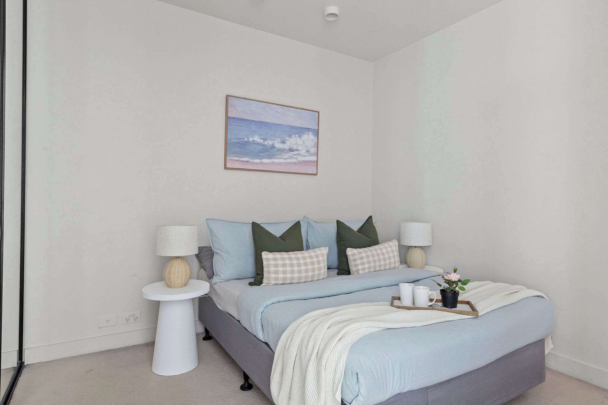A bedroom with a bed, bedside tables, a lamp, a tray with a plant, and a painting on the wall.