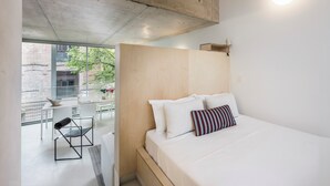 A modern hotel room with a large bed, a wooden headboard, a dining area with a table and chairs, and a view of the outside. - Edmond Vibes Avenida de América (Madrid)
