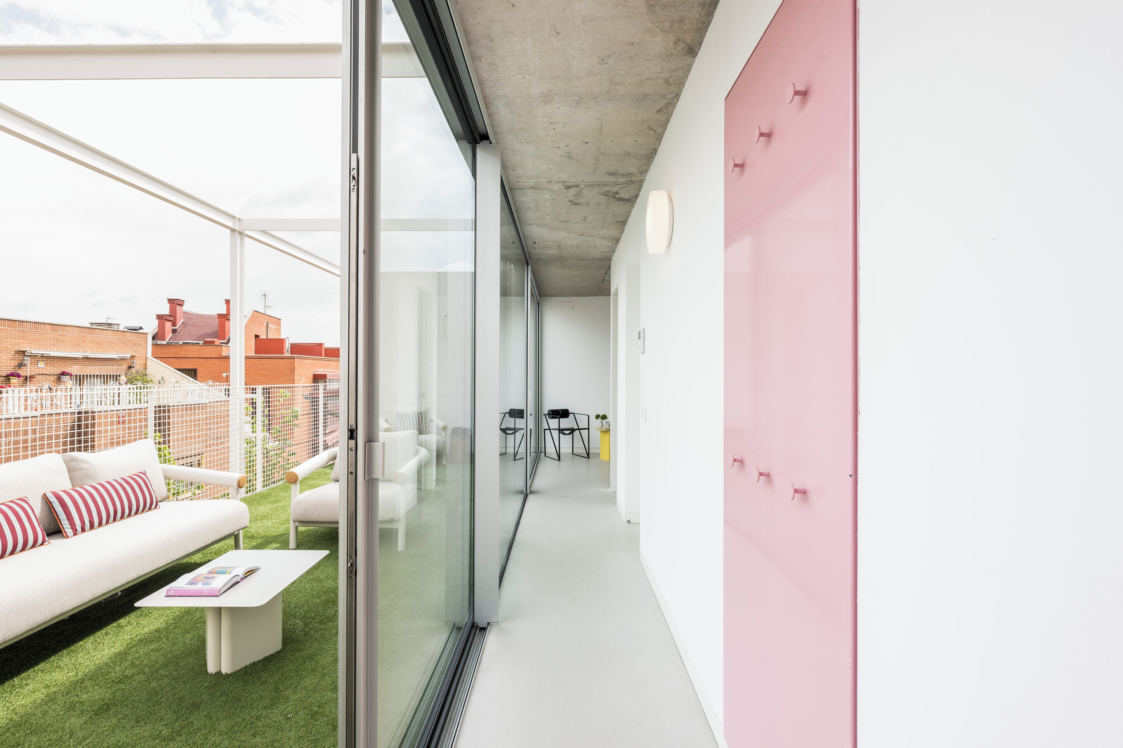 Een modern interieur met een glazen wand, een witte bank en een roze muur.