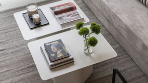 Two white side tables with books, candles, and a vase with green spherical objects. - Edmond Vibes Avenida de América (Madrid)