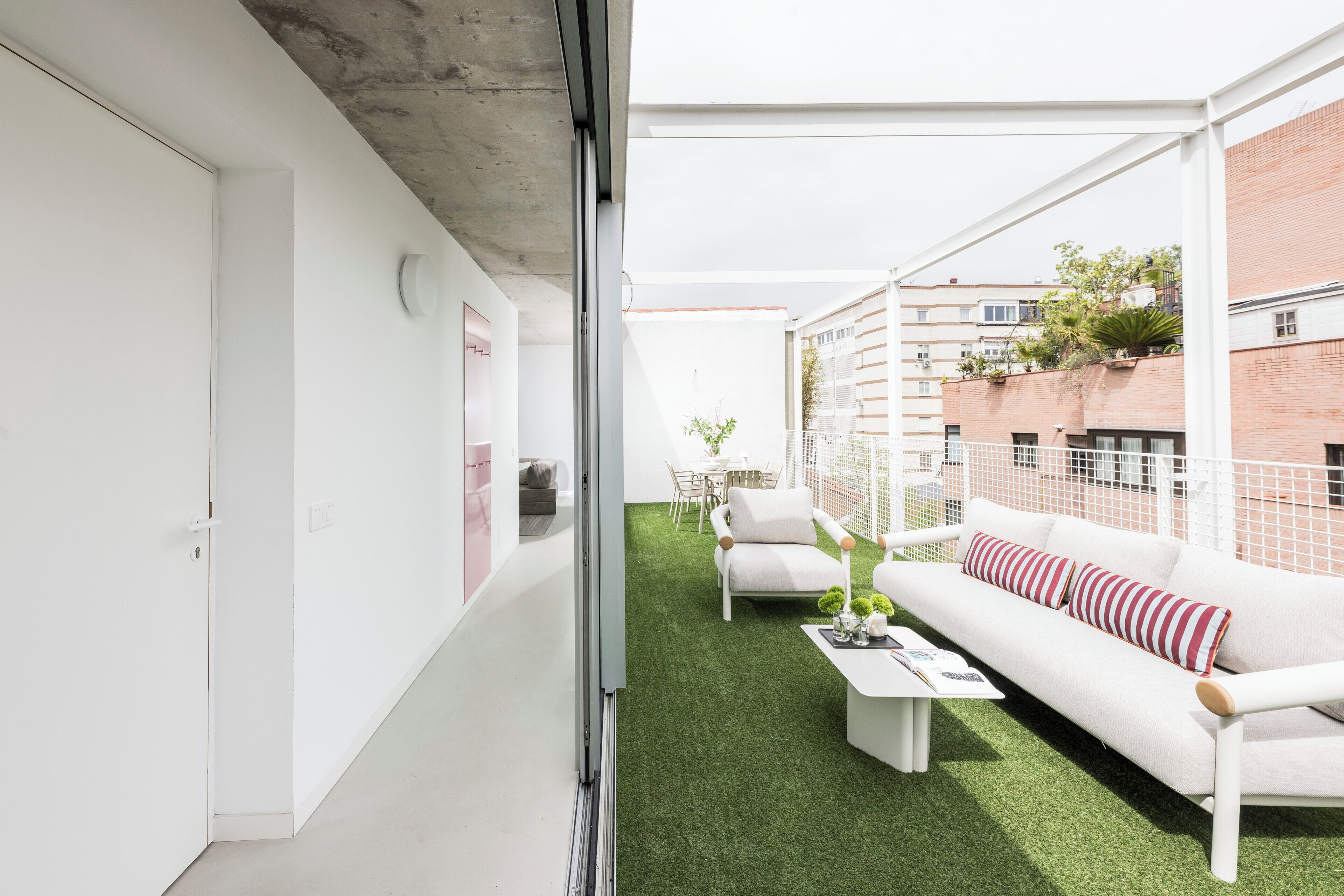 Un apartamento moderno con interior blanco, piso de césped artificial verde, sofá blanco con almohadones a rayas y una mesa de centro blanca.