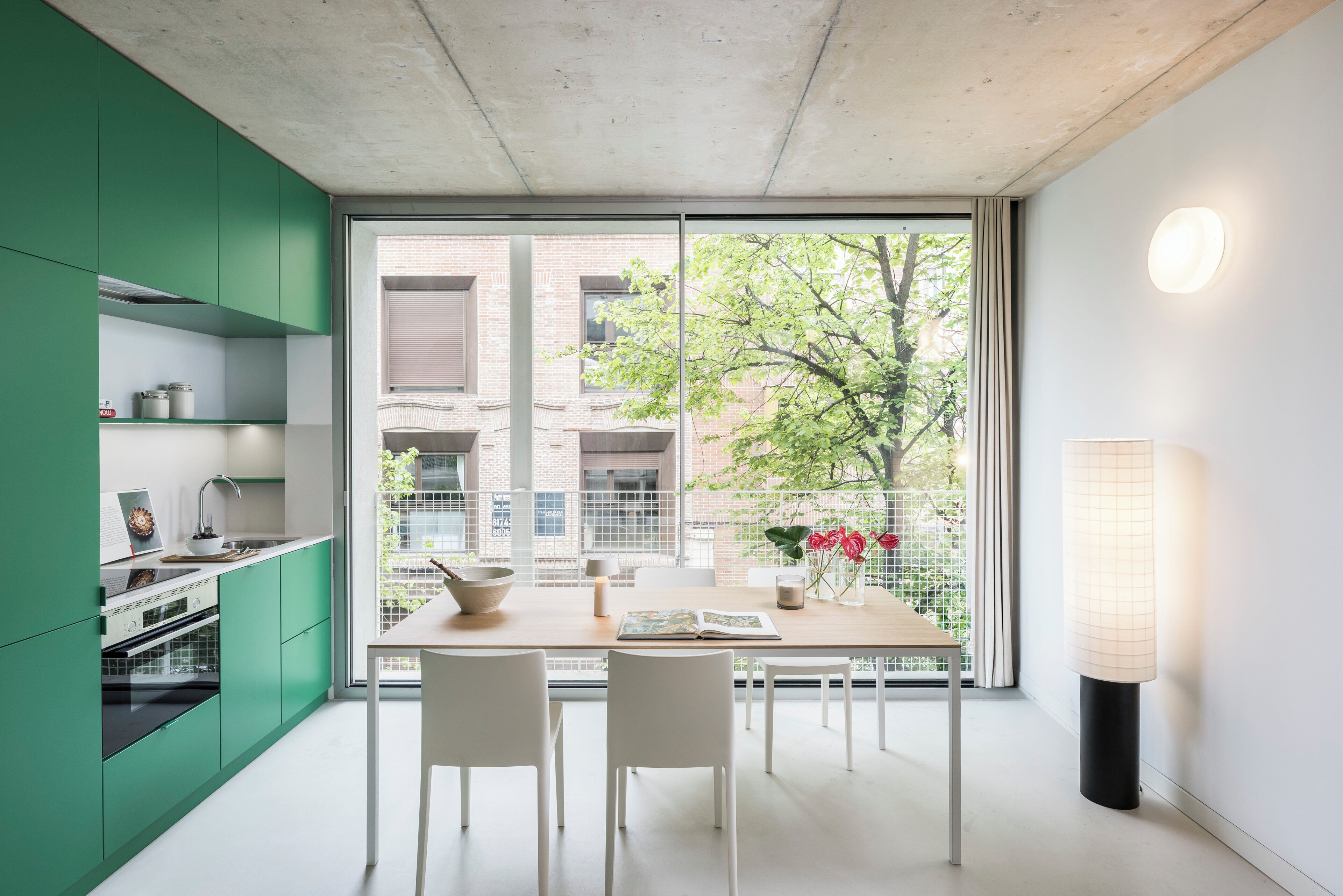 Une cuisine moderne avec des meubles de couleur verte, une grande fenêtre et un coin repas comprenant des chaises et une table.